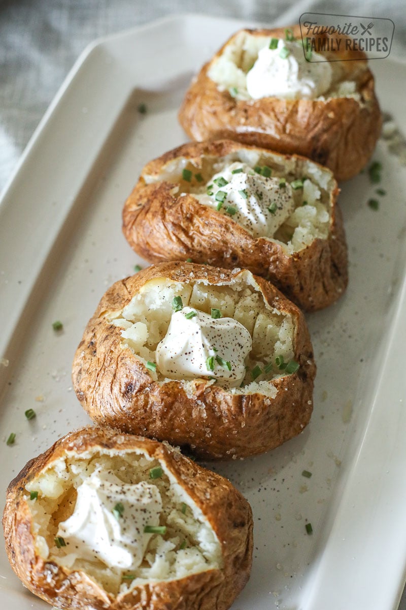 Four baked potatoes on a platter with sour cream and chives.