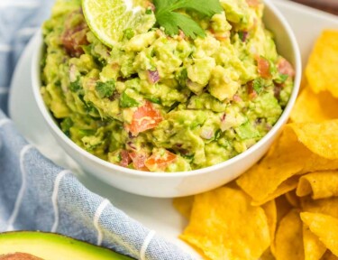 Guacamole in a small bowl topped with a lime slice and a cilantro leaf