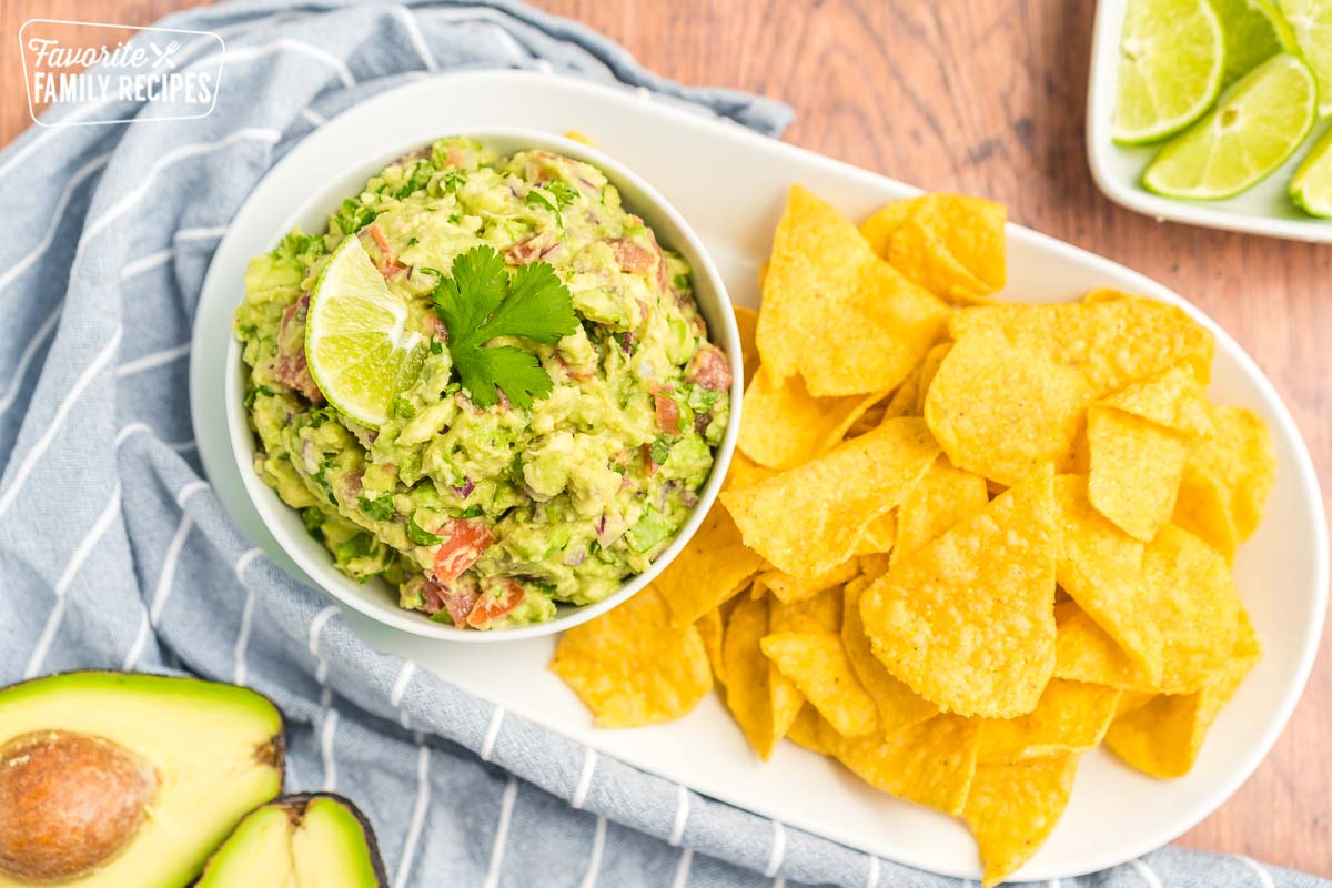 A small bowl of guacamole topped with a slice of lime and a cilantro leave. The bowl is next to a pile of tortilla chips.