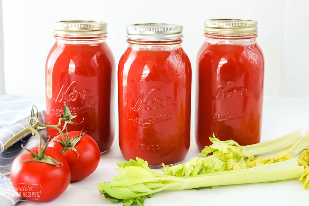Three quart jars of canned tomato juice with tomatoes and celery stalks