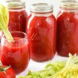 Three quart jars of tomato juice and a glass of tomato juice with a celery stalk in it for garnish.