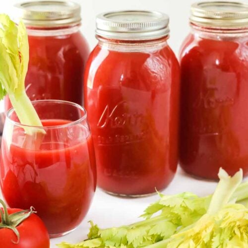 Three quart jars of tomato juice and a glass of tomato juice with a celery stalk in it for garnish.