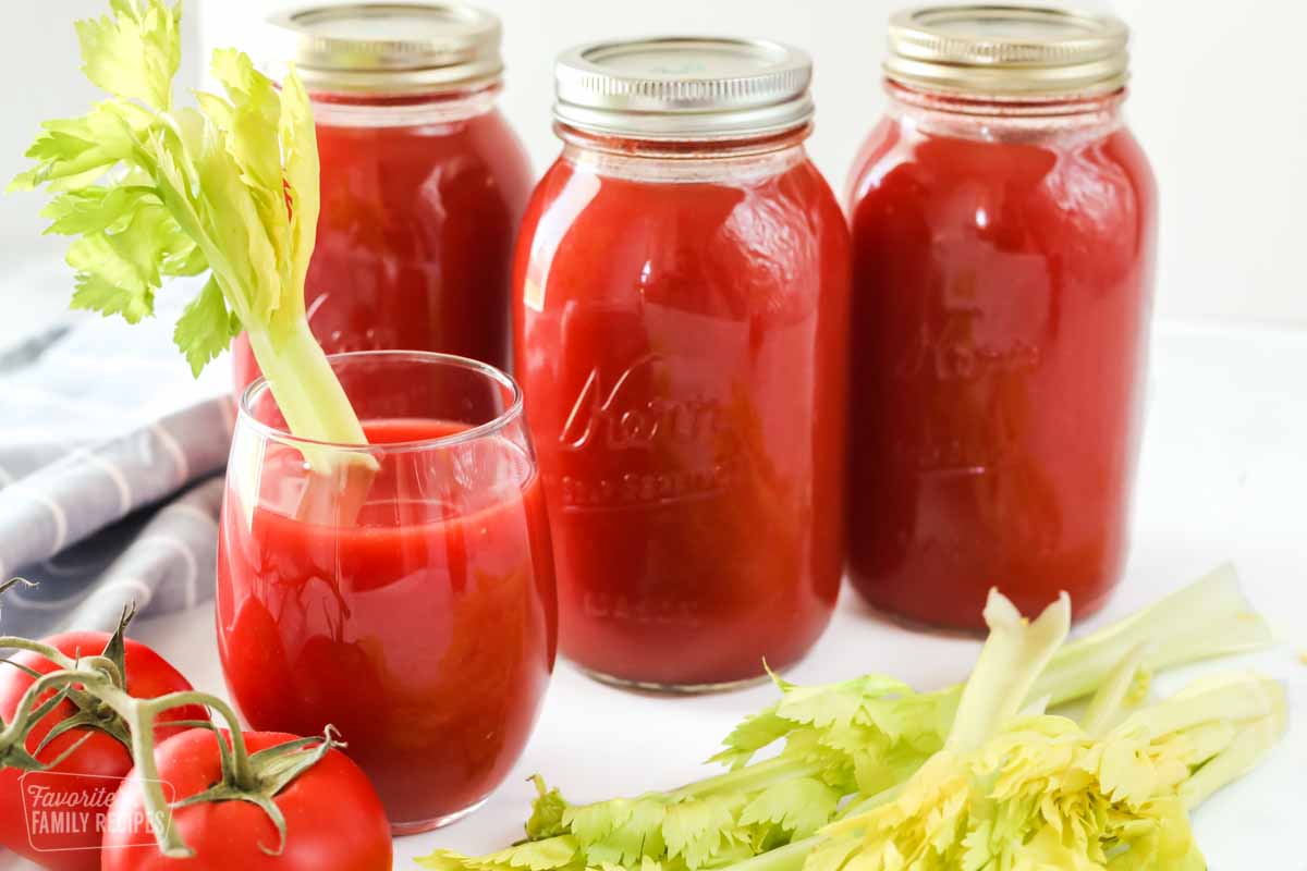 Three quart jars of tomato juice and a glass of tomato juice with a celery stalk in it for garnish.