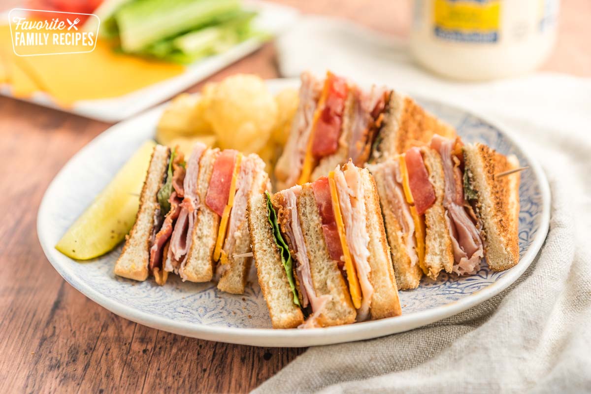 A club sandwich served on a plate with potato chips and a pickle