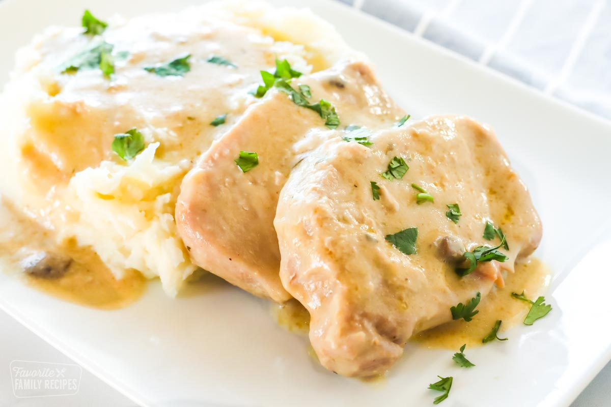 Pork chops made in a crock pot and mashed potatoes with gravy on a plate.