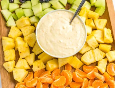 A bowl of fruit dip surrounded by fruit