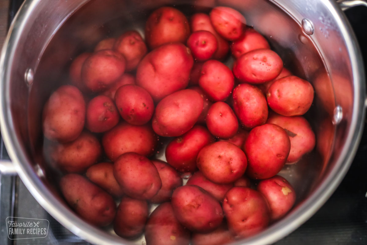 Small red potatoes in a bot of water on a stovetop.