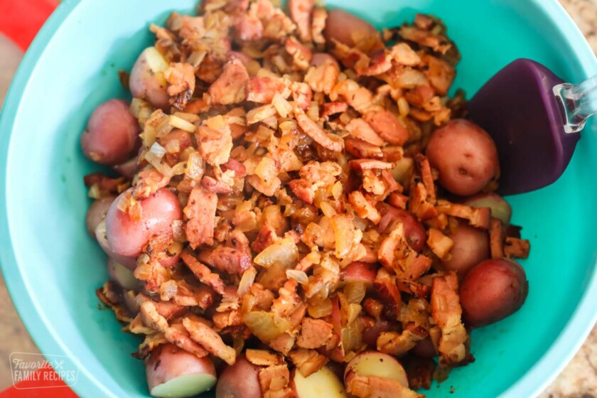 Red potatoes being tossed with bacon, onion, and vinegar to make German Potato Salad.