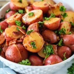 A bowl of halved red potatoes with a bacon vinegar glaze, garnished with parsley and bacon bits combined to make German Potato Salad.