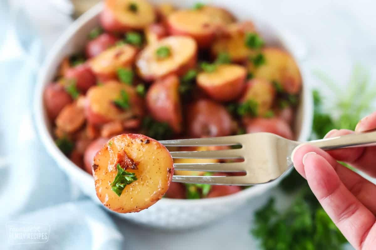 A piece of a red potato on a fork. A bowl of German potato salad is in the background.