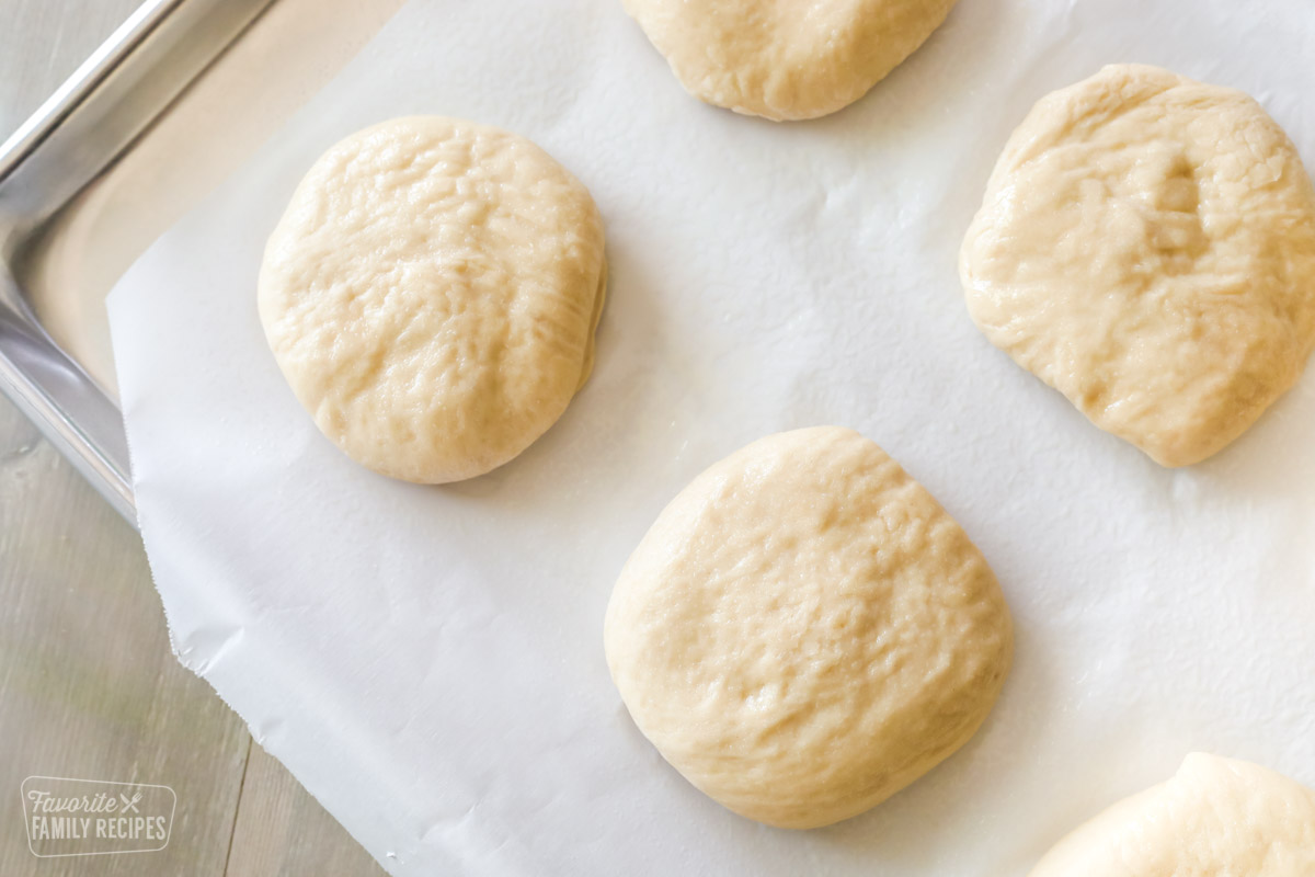 Dough formed into flat round shapes forming a bun and placed on a baking sheet