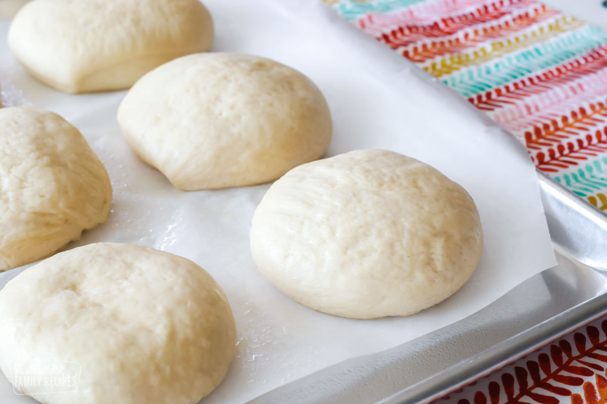 Hamburger dough on a baking sheet that has been formed into buns and has risen and is ready to bake.