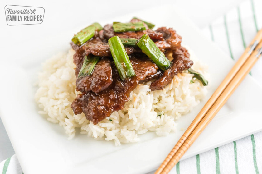 Mongolian Beef topped with green onions on a bed of rice with chopsticks next to the plate.