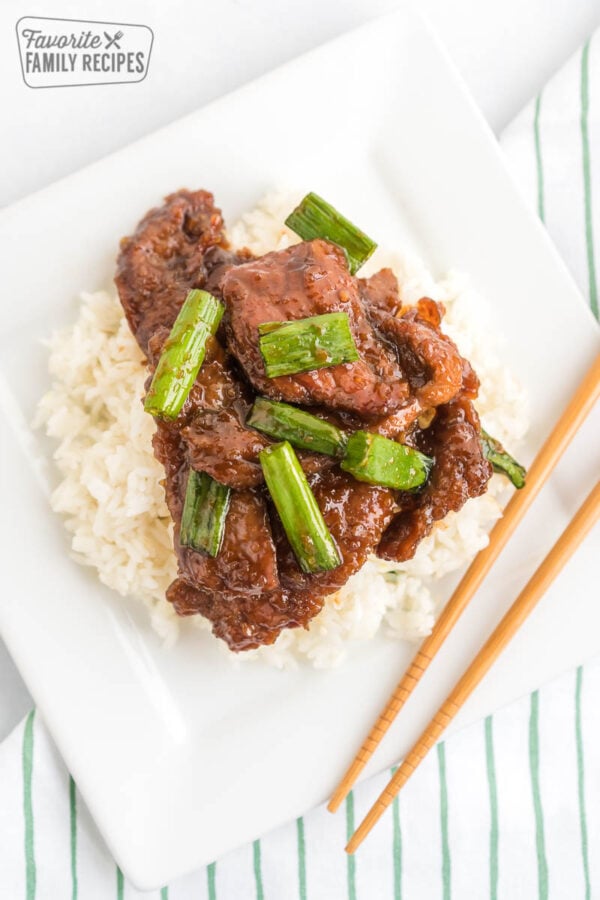 Mongolian Beef topped with green onions on a bed of rice with chopsticks next to the plate.