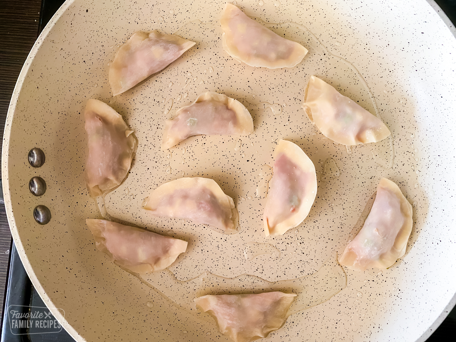 Ten uncooked potstickers being cooked in oil in a skillet