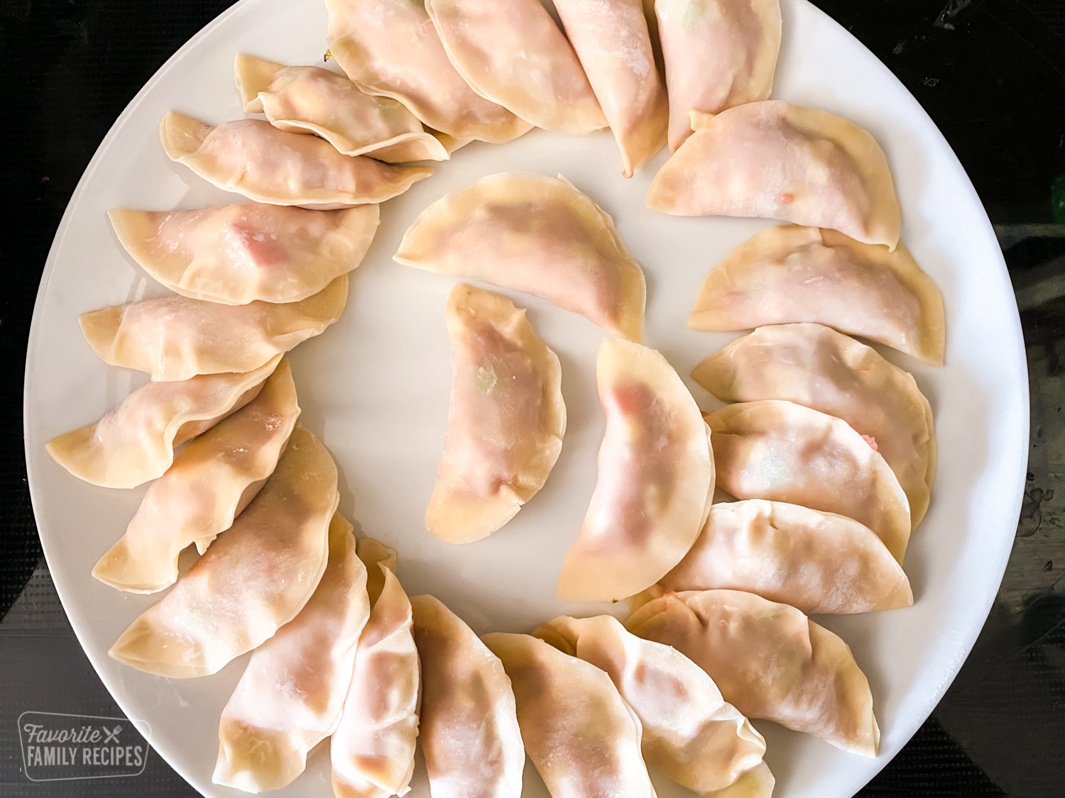 A large plate of uncooked potstickers that have been placed overlapping in a circle.