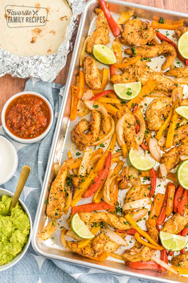 Sheet Pan fajitas with tortillas, salsa, sour cream, and guacamole on the side