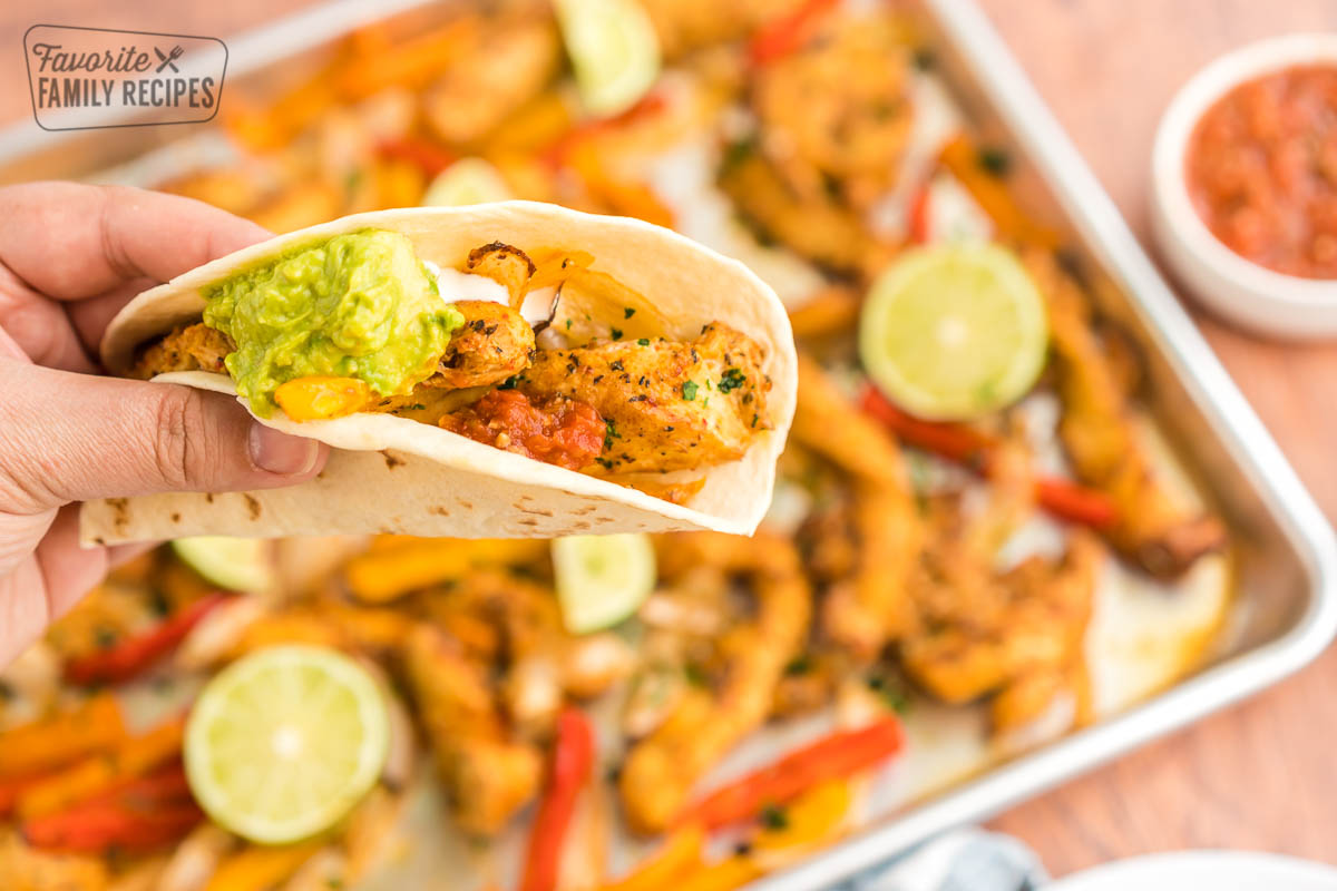 A fajita being held above a pan of sheet pan fajitas for a dinner idea