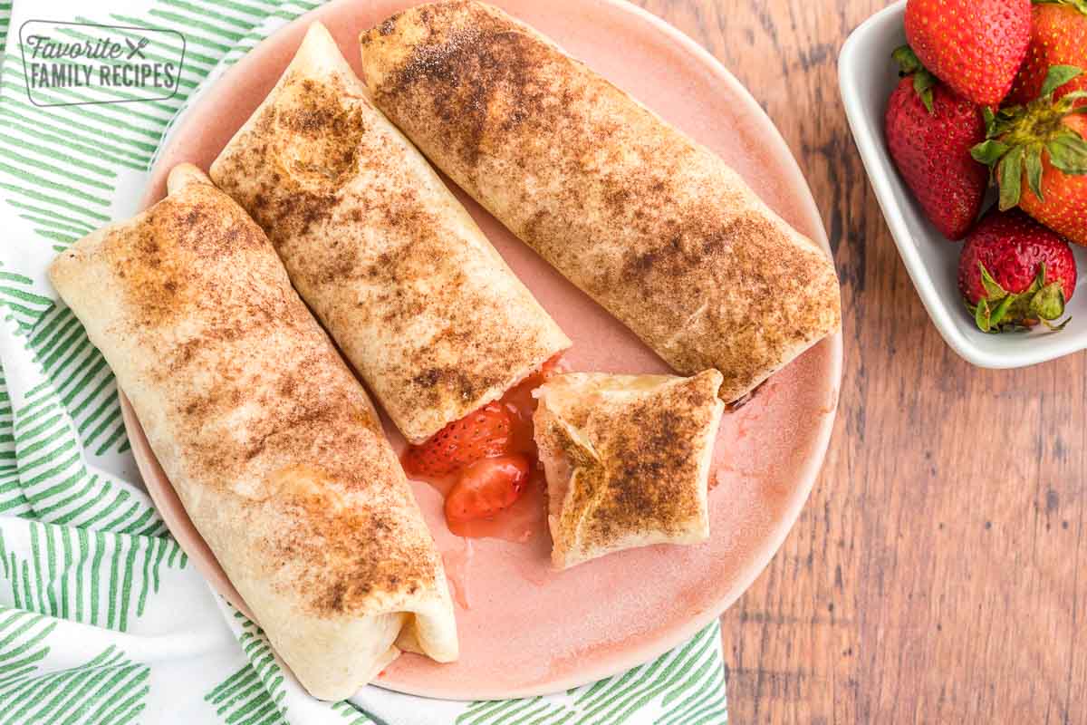 Three strawberry empanadas on a plate next to a bowl of strawberries