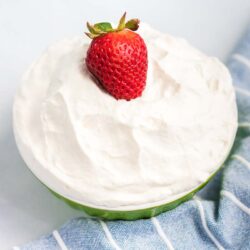 A strawberry on top of a bowl of whipped cream