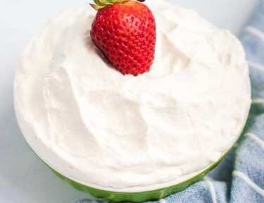 A strawberry on top of a bowl of whipped cream