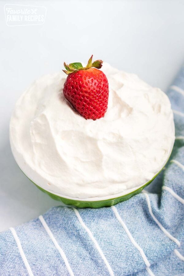 A strawberry on top of a bowl of whipped cream