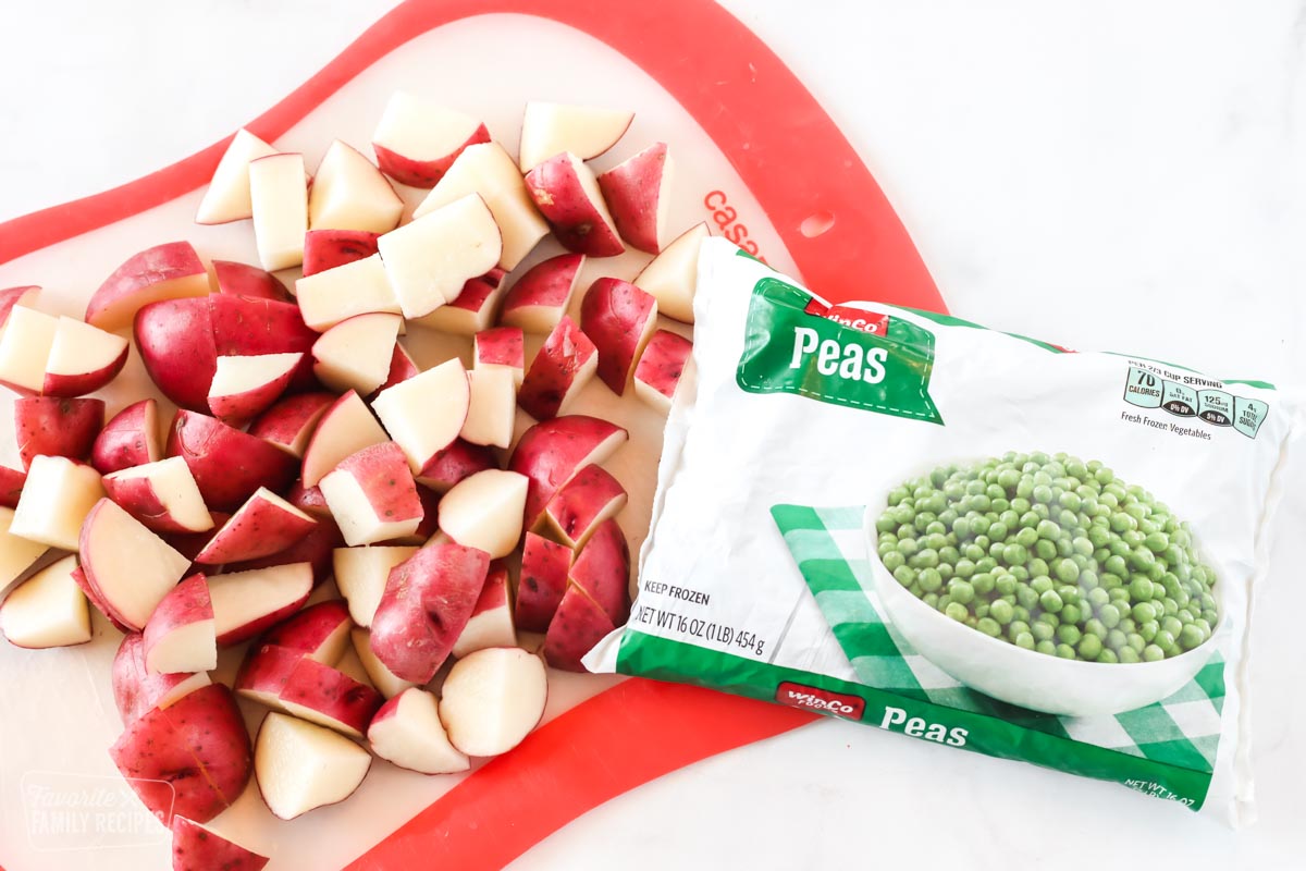 Diced red potatoes on a cutting board next to a package of frozen peas