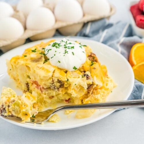 A white plate with a serving of crockpot breakfast casserole with a dollop of sour cream on top