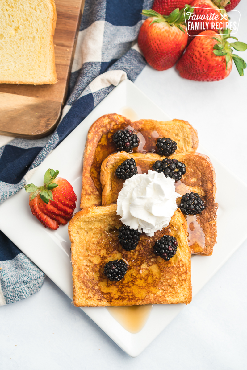 French toast with syrup, whipped cream, and fresh fruit on a white plate. 