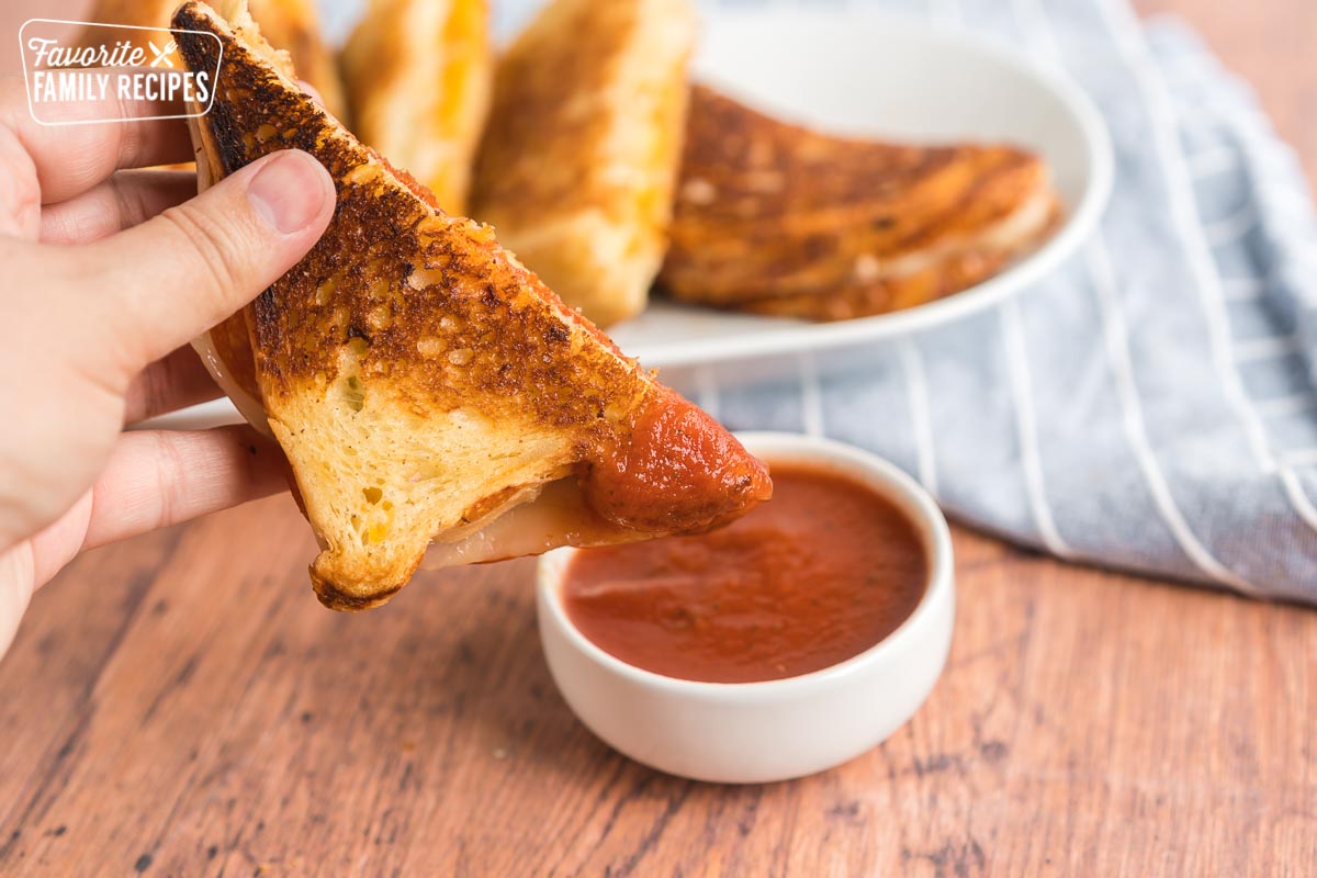 A sandwich being dipped in marinara sauce.