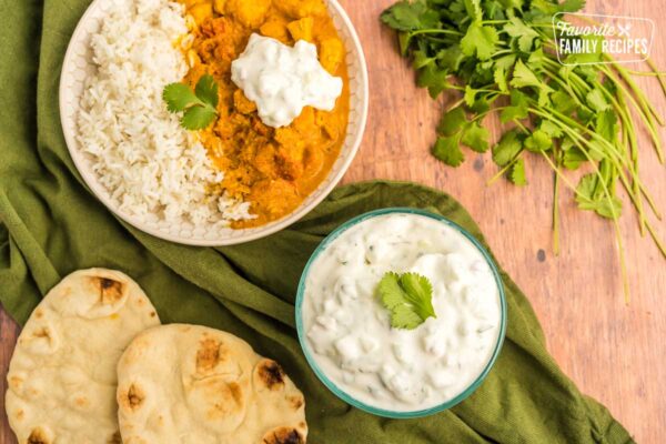 Bowls of rice, chicken tikka masala, and raita on a table with naan bread