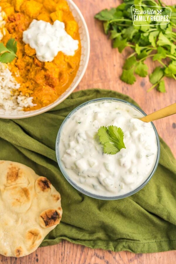 Bowls of rice, chicken tikka masala, and raita on a table with naan bread