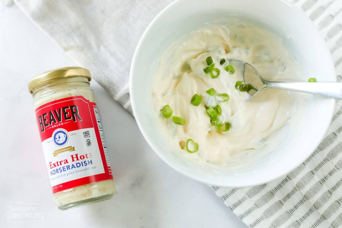 A bowl of horseradish cream next to a jar of horseradish.