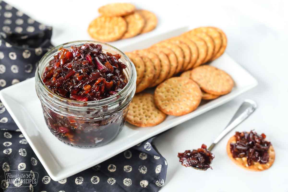 Bacon jam in a jar next to a plate of crackers.