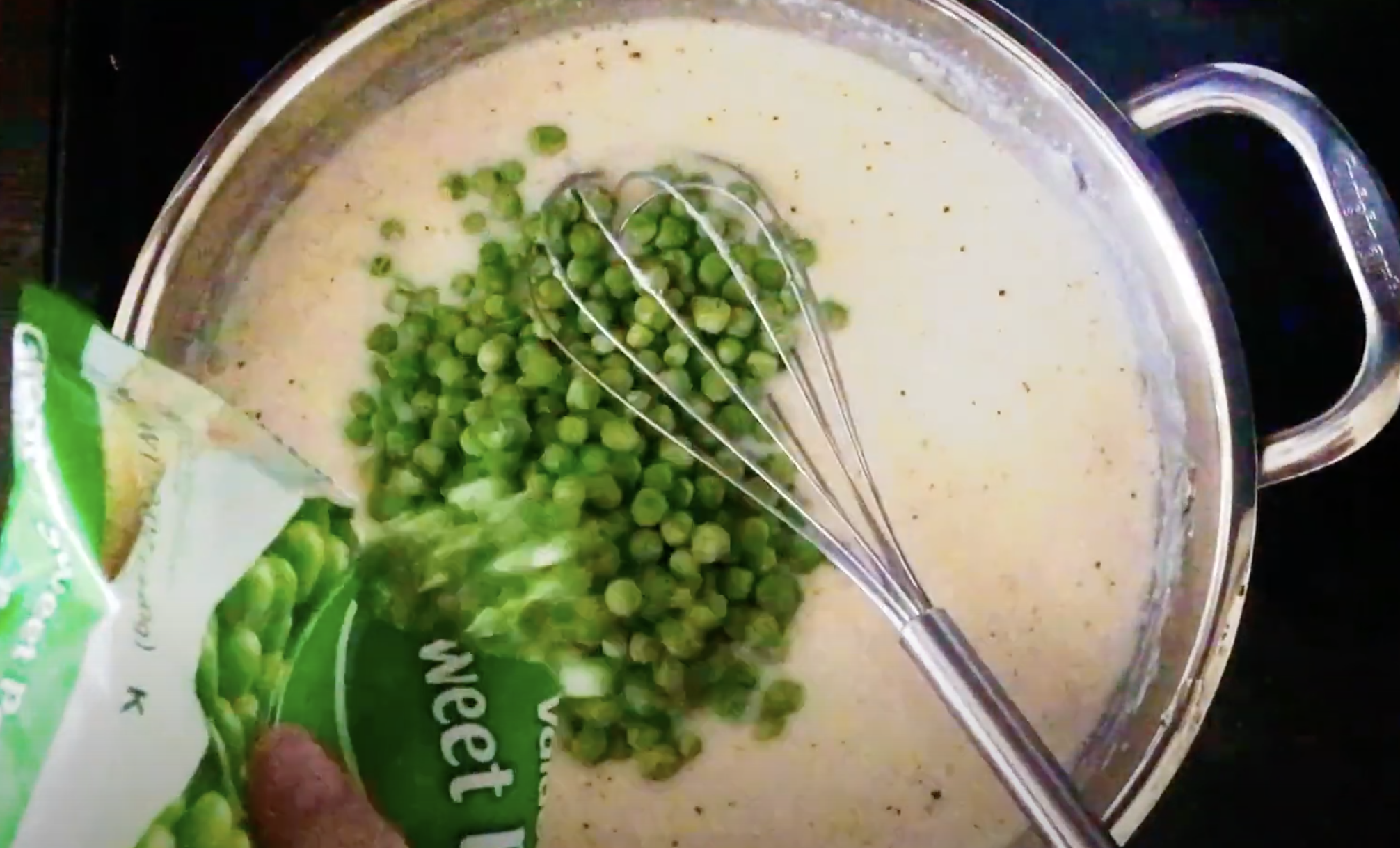 Peas being stirred into cream sauce in a skillet.