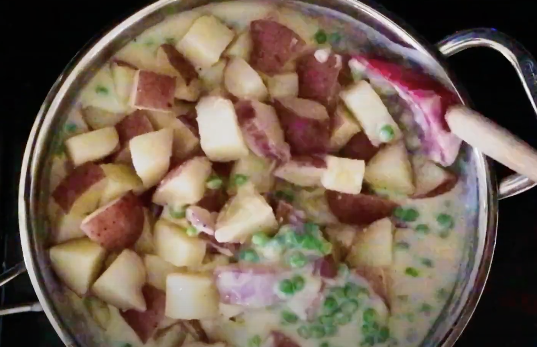Red potatoes being stirred into a skillet with peas and cream sauce.