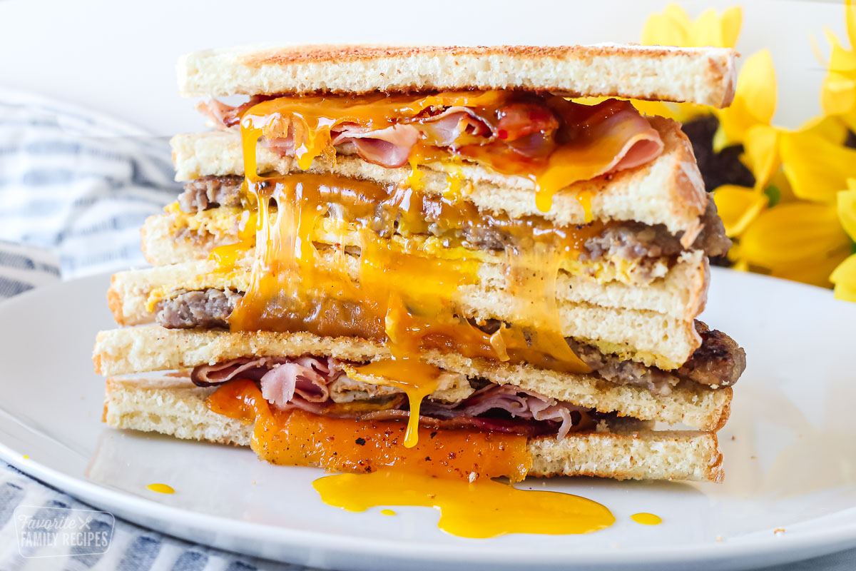 A breakfast sandwich cut inhale and stacked. It is a close-up view to show cheese, egg yolk, sausage, bacon, and ham.