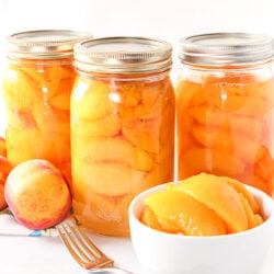 Three bottles of canned peaches and a bowl of peeled, sliced peaches