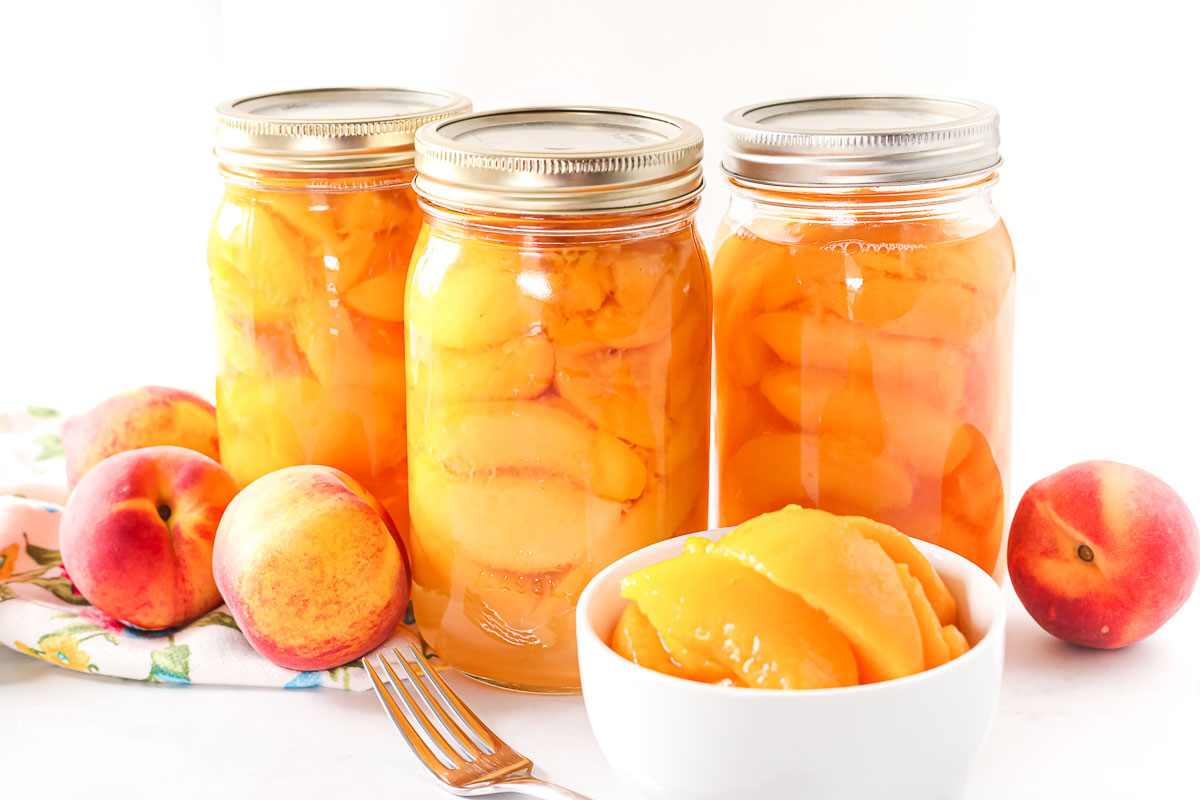 Three bottles of canned peaches and a bowl of peeled, sliced peaches.