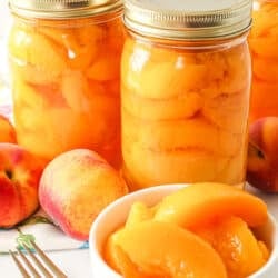 A bowl of sliced peaches in front of bottles of peaches