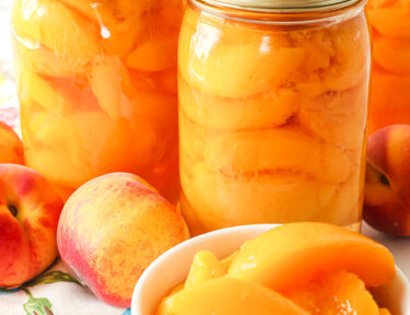 A bowl of sliced peaches in front of bottles of peaches