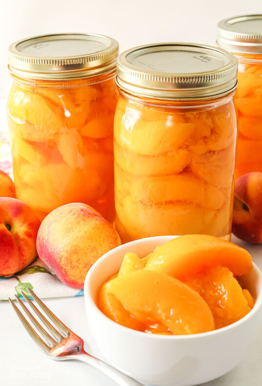 A bowl of sliced peaches in front of bottles of peaches