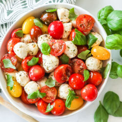 A top-view of a bowl of caprese salad with cherry tomatoes, mozzarella, basil and seasonings.