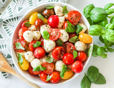 A top-view of a bowl of caprese salad with cherry tomatoes, mozzarella, basil and seasonings.