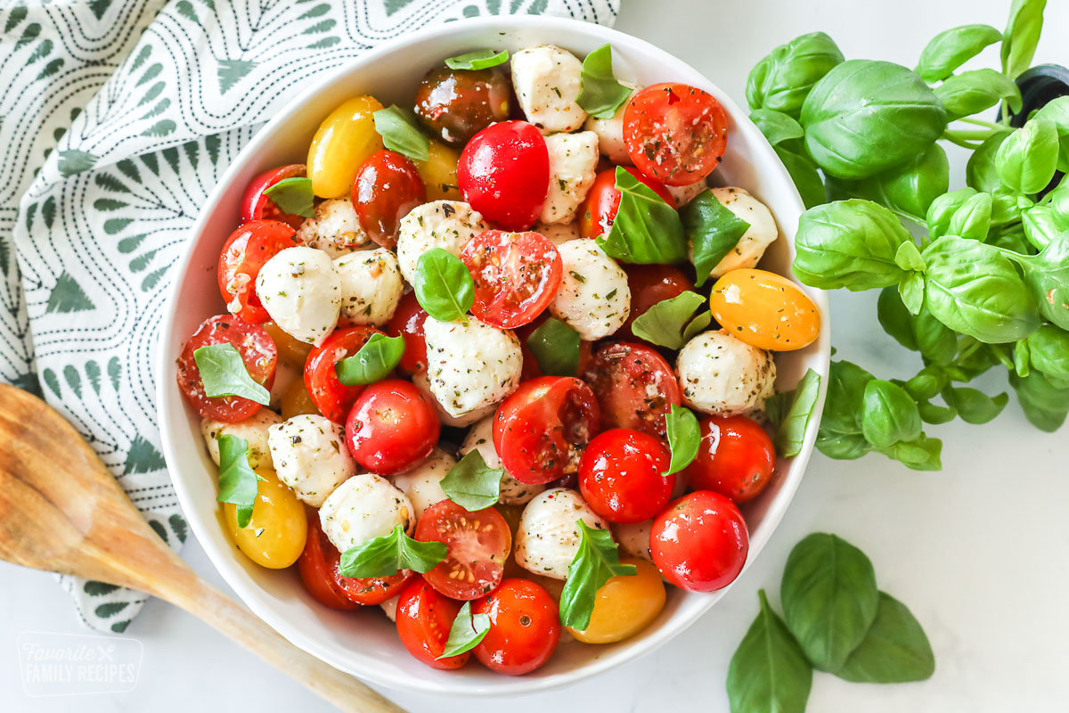 A top-view of a bowl of caprese salad with cherry tomatoes, mozzarella, basil and seasonings.