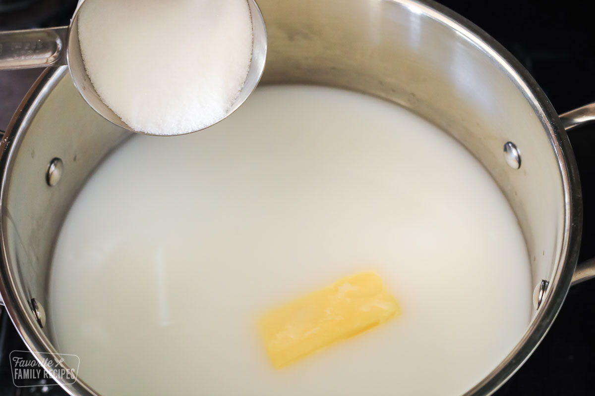 Sugar being poured into a pot with milk, water, and butter.