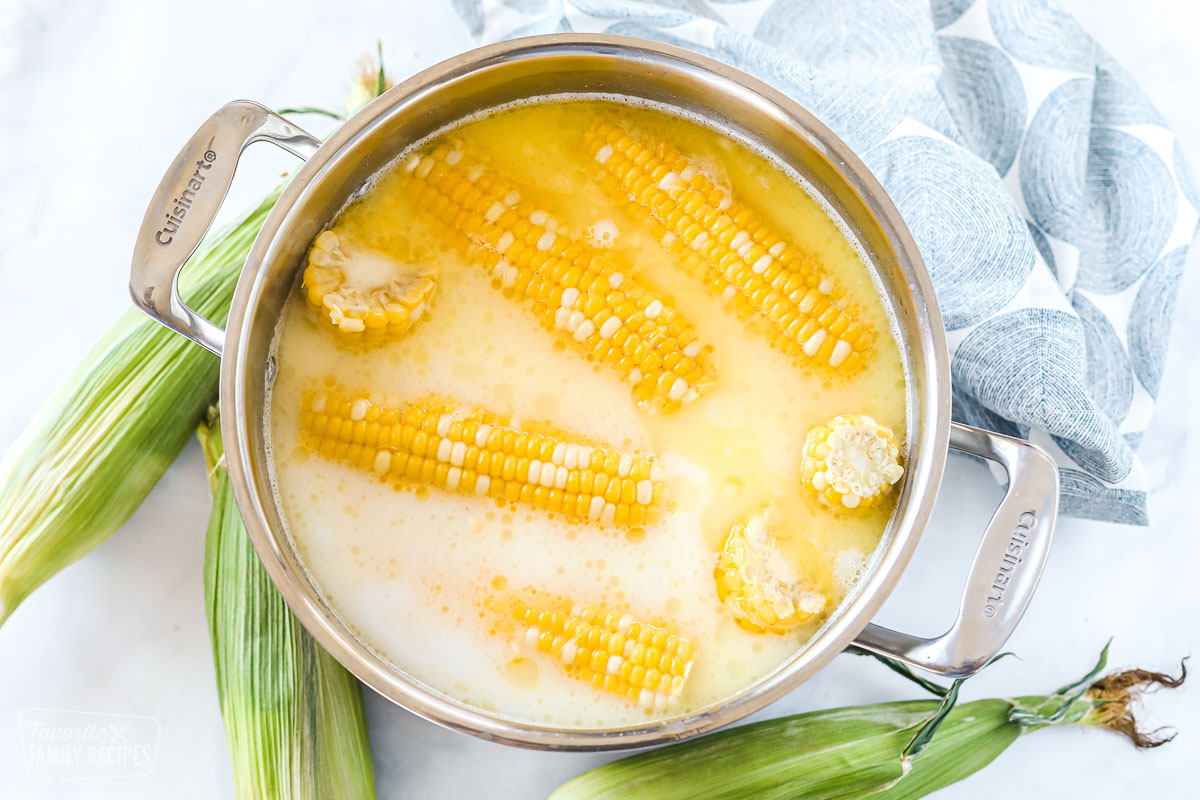 Five ears of corn that have been shucked and are in a pot of water, milk, and butter waiting to be cooked.