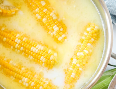 Six pieces of sweet corn in a pot with water, milk, and butter