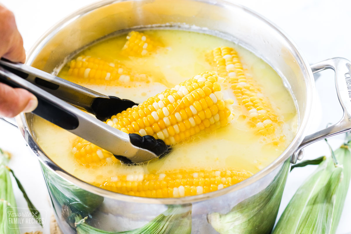 Corn on the cob in a stock pot. One piece is being puled out with a pair of tongs.