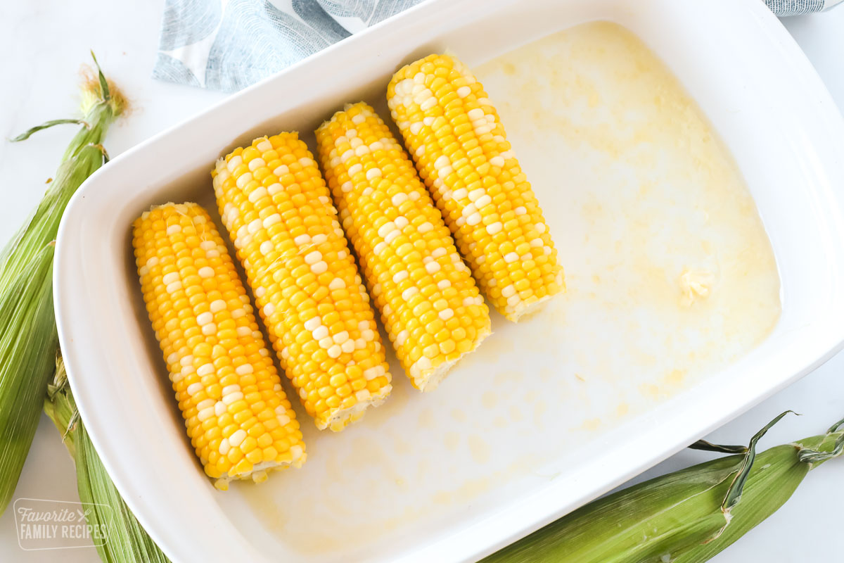 Four pieces of peeled corn on the cob in a dish with melted butter